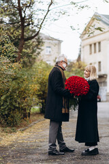Fototapeta premium Elderly couple, handsome old man gives a huge bouquet of red flowers to his lady on a valentines day