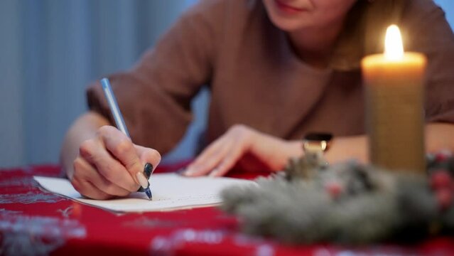 A woman writes down plans for the new year near the Christmas tree. Holiday planning happiness Santa Claus letter adult girl. High quality 4k footage