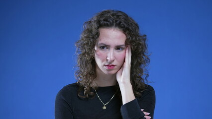 Preoccupied woman feeling anxiety while standing on blue background. Close-up face of person...