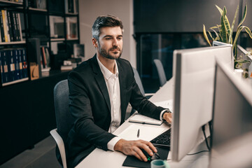 A creative director is using computer at his office while looking at monitors.