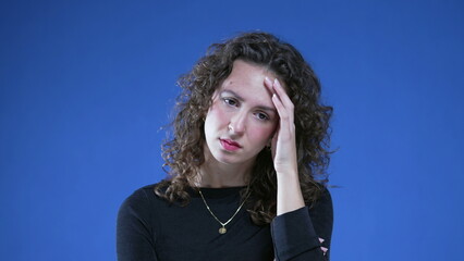 Preoccupied woman feeling anxiety while standing on blue background. Close-up face of person...