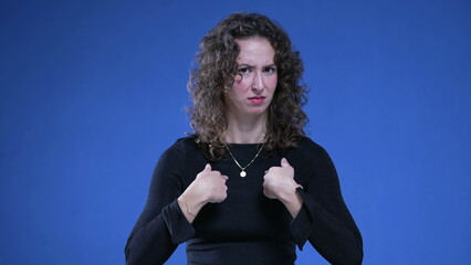 Woman pointing at herself in confusion with finger in disbelief and consternation standing on blue...
