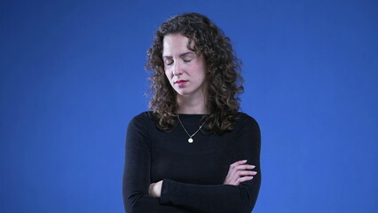 Upset woman with arms crossed looking at camera with angry expression, standing on blue background....