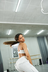 Fototapeta na wymiar young long-haired african american dancer in white sportswear rehearsing in modern dance studio
