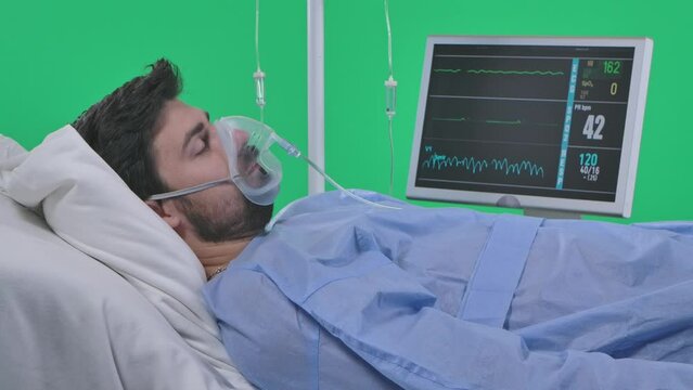 Close shot man in bed with drip and monitor, loses consciousness, heart rate stops, hand falls. Isolated on chroma key green screen.