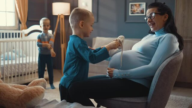 Little boy holding Small shoes for unborn baby on belly at his pregnant mother 