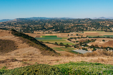 An aerial landscape unveils rolling hills, a patchwork of vibrant agricultural fields, and the quaint silhouettes of houses against the horizon