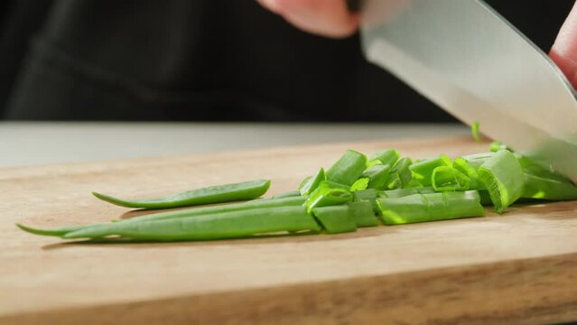 Chef cutting Bunch of green onion feathers by knife on a cutting board on professional restaurant kitchen, Close-up macro rotating shot. 