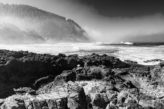 Fog and mist along the rocky mountain coastal area and beach of the Pacific Ocean central Oregon coast converted to classic black and white image. 