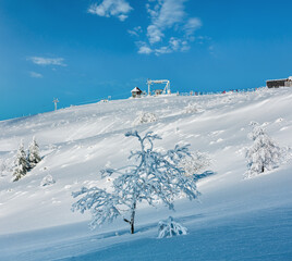 Morning winter calm mountain landscape with beautiful frosting trees, snowdrifts on slope and ski lifts in far (Carpathian Mountains, Ukraine). Skiers are unrecognizable.