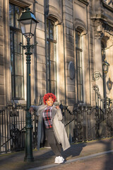Female model with strong unique style appearance in urban wealthy inner city street lamp iron fence environment. Confident curvy black lady stylish red hair with winter good taste fashion
