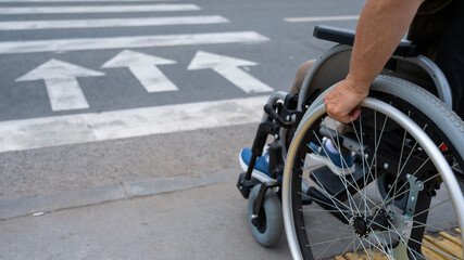 Fototapeta premium Rear view of an elderly woman in a wheelchair going to a pedestrian crossing. Close-up on wheels. 