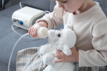 A little girl treats a toy lamb with a needle. Playing doctor with soft toys. nebulizer, treatment of colds of the upper respiratory tract.