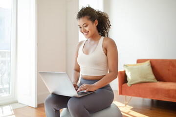 Athletic young woman using laptop for online training videos indoors
