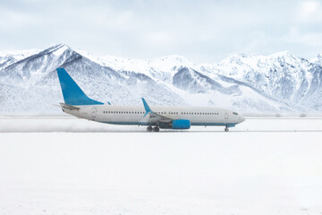A passenger airliner moves on the runway in a severe snowstorm on the background of high snow...