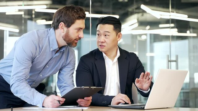 Two diverse colleagues discussing new project, businessmen using digital tablet and laptop compter together in office. professional man corporate employees in conversation working on business project