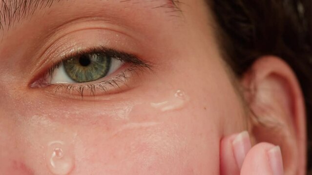 Young woman applying hydrogelic serum cream on her face close-up. Morning skin care routine. Pink background