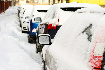 Row of parked snowy cars on snowy street, cars covered with fresh snow