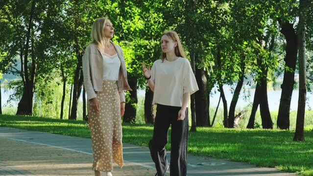 Family of mother and daughter starts conflict walking in summer city garden. Woman obviously frustrated by behavior of teenage girl