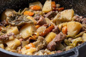 Delizioso spezzatino con carne di maiale, patate, carote, pomodori secchi e carciofi, cibo italiano 