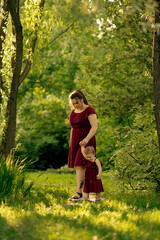 A mother lifts her child high in the air, a shared moment of joy under the canopy of a sunlit grove, their laughter mingling with the whispers of leaves.