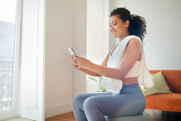 Young fit woman browsing workout apps on cell phone indoor - obrazy, fototapety, plakaty