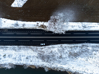 Top down aerial photo of a straight road going trough the snowy forest and agricultural land