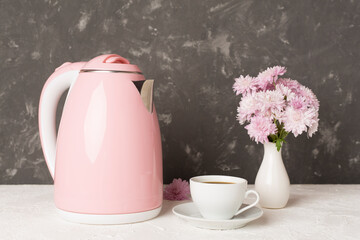 Pink electric kettle with cup of tea and dessert on table