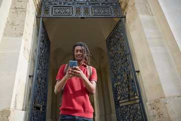 Male Student Checking Messages Or Social Media On Mobile Phone Outside University Building In...