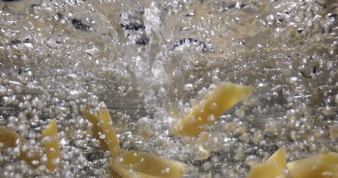 Cooking pasta penne. Chef throwing raw spaghetti into boiling water in pot on kitchen stove. Italian cuisine, food preparation, cook blog. View from the side