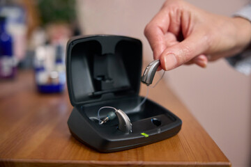 Close Up Of Person Picking Up Wireless Hearing Aid Or Device From Charging Case At Home