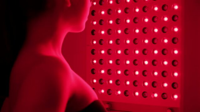 Red light therapy. The woman in black bikini goes of skin rejuvenation with the help of red light treatment. Close up
