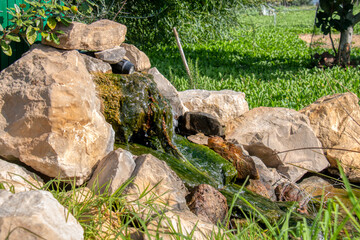 Fountain with rocks with verdigris from which the water flows decorating a garden.