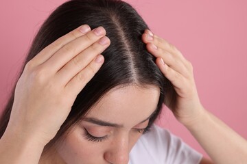 Woman examining her hair and scalp on pink background, closeup