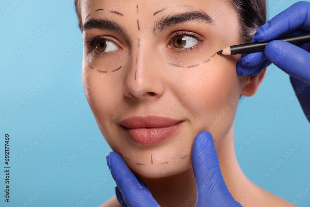 Canvas Prints Doctor drawing marks on woman's face for cosmetic surgery operation against light blue background, closeup