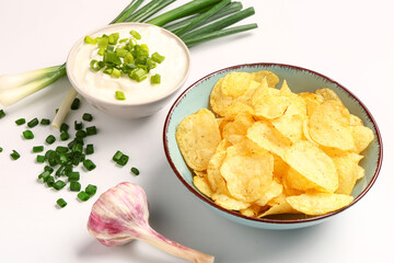 Bowl of tasty sour cream with sliced green onion and potato chips on white background