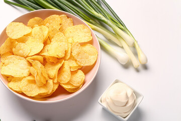 Bowl of tasty sour cream with green onion and potato chips on white background