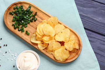 Bowl of tasty sour cream and sliced green onion with potato chips on blue wooden background