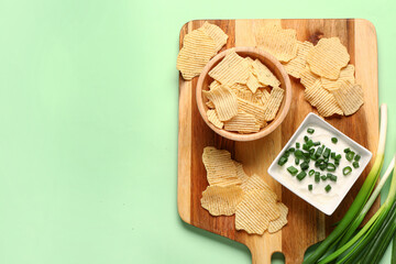 Fototapeta na wymiar Bowl of tasty sour cream with sliced scallion and potato chips on green background