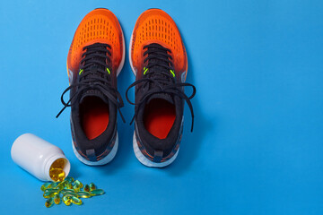 Orange sports sneakers and vitamin D pills and omega 3 capsules poured out of a jar on a blue background