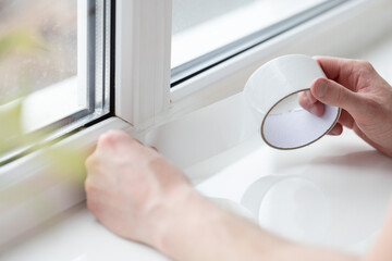 Man putting draught excluder tape on window, protection from the draft.