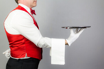 Portrait of Waiter in Red Vest or Waistcoat and Red Bow Tie Holding Silver Serving Tray. Concept of Service Industry and Professional Hospitality.
