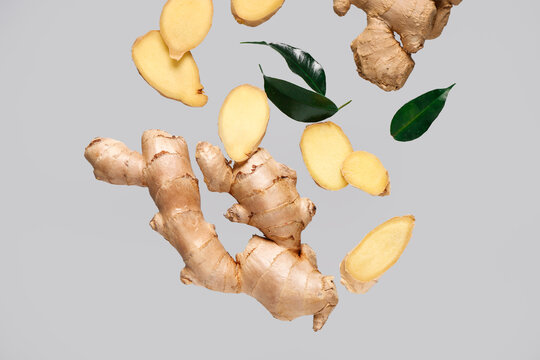 Flying slices of fresh ginger root and leaves on grey background
