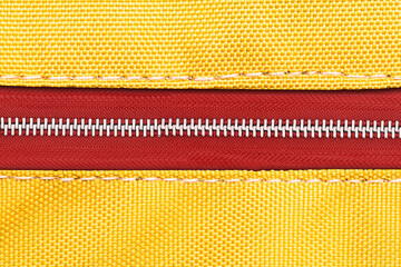 Yellow fabric red metal zipper. Vibrant color style clothing accessories. Sewer element background. Closed zipper. Zipped zipper. Silver gray shiny zipper teeth background. © Paweł Michałowski