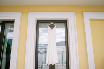 Bridal dress hangs on a hanger on the hotel balcony door