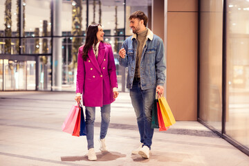 Joyful European husband and wife carry shopper bags outdoor mall