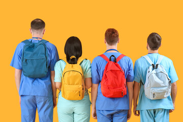 Group of medical students with backpacks on yellow background, back view - obrazy, fototapety, plakaty