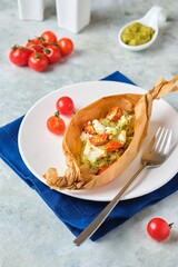 Fish baked with pesto sauce, cherry tomatoes and feta in portioned parchment forms on a white plate on a gray concrete background. Fish recipes.