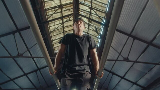 Low angle view of strong male athlete performing dips and l-sits combo on parallel bars in training gym