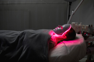 Woman getting cosmetic procedure with LED facial mask. , photon therapy - obrazy, fototapety, plakaty
